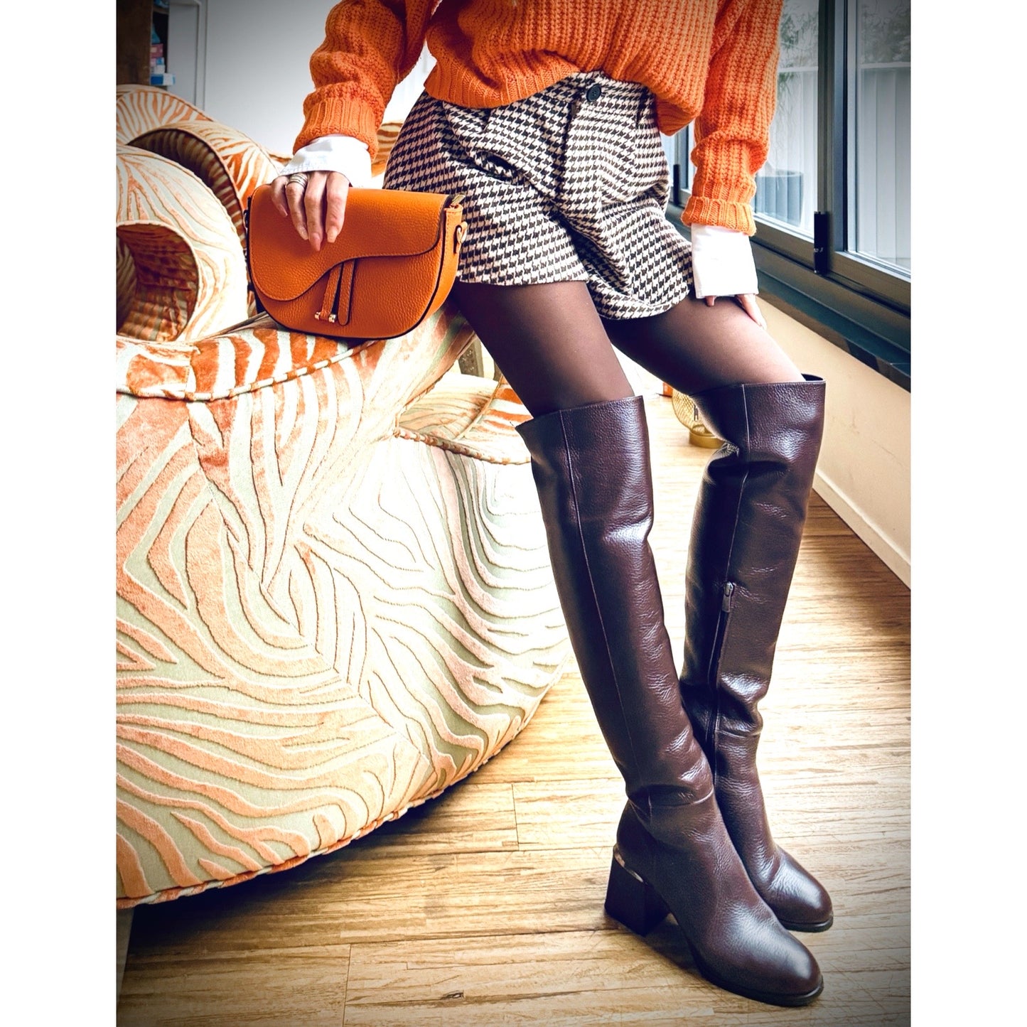 Handbag Dion Orange – LiBEAU Damen hält orange Leder Umhängetasche Dion zu orangenem Strickpullover, Hahnentritt-Minirock und dunkelbraunen Knieboots, selbstbewusster herbstlicher Editorial Look | LiBEAU