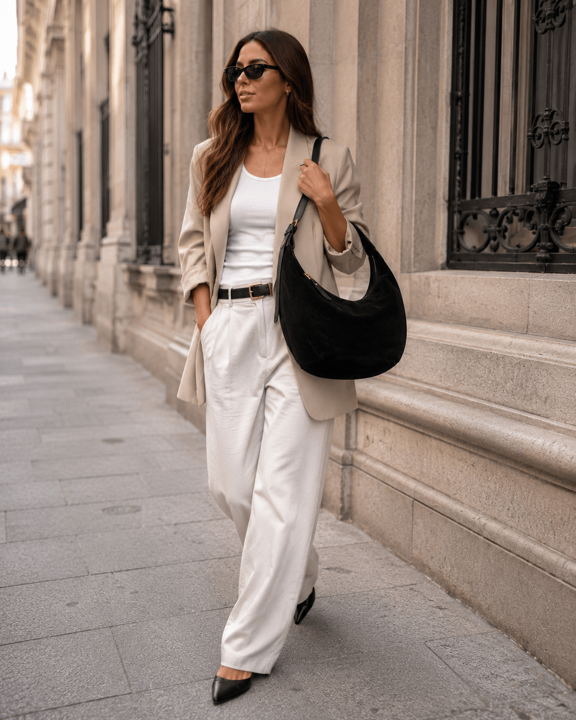 Bag Sauvage – LiBEAU Damen trägt schwarze Wildleder Hobo Bag über der Schulter zu beigem Oversized-Blazer, weißem Tank-Top und cremefarbener Weithose auf Madrider Boulevard, zeitloser selbstbewusster City Editorial Look | LiBEAU
