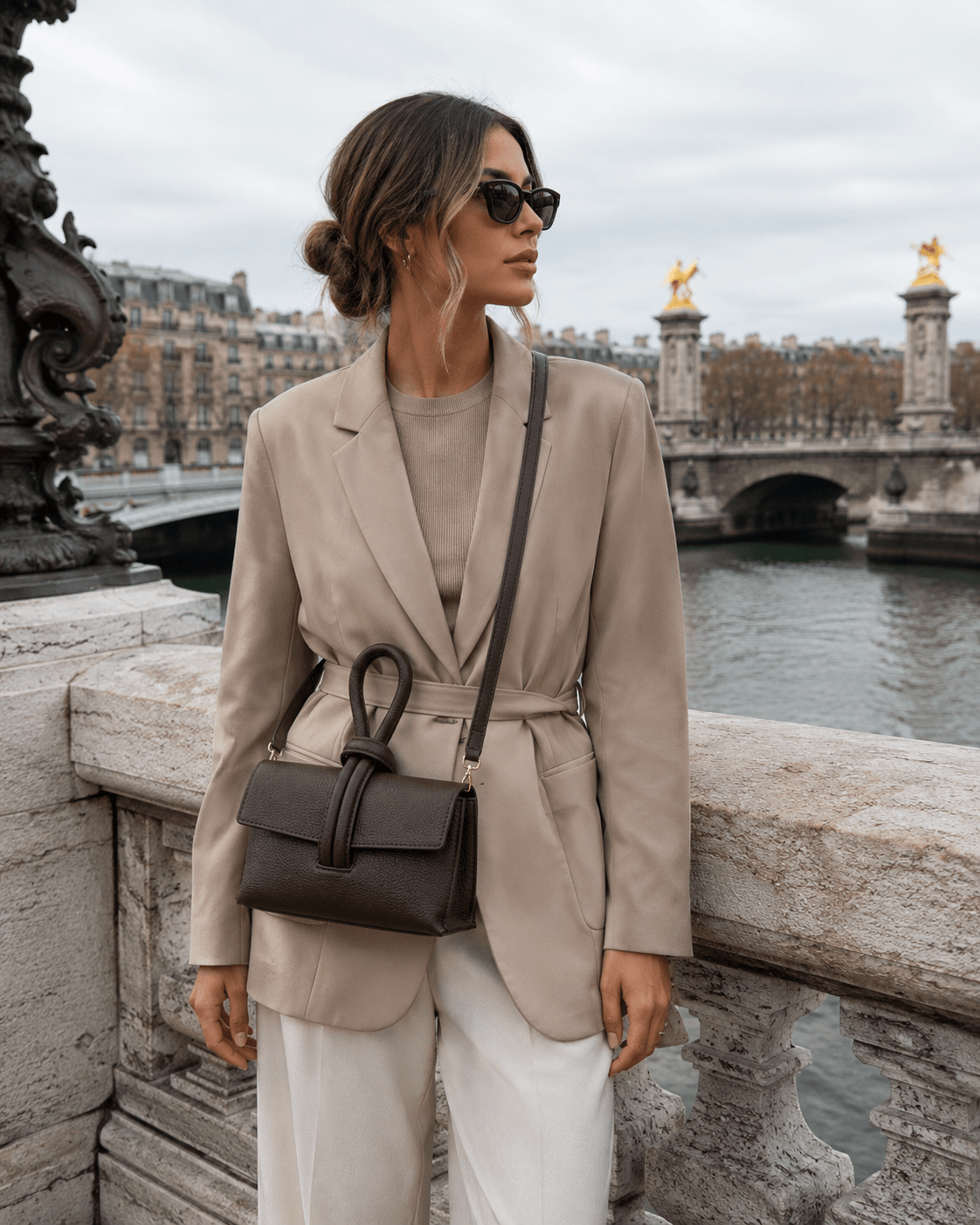 Clutch Michelle Choco – Frau trägt dunkelbraune Leder Clutch als Umhängetasche, eleganter Pariser Streetstyle mit beigem Blazer und weißer Hose auf der Brücke
