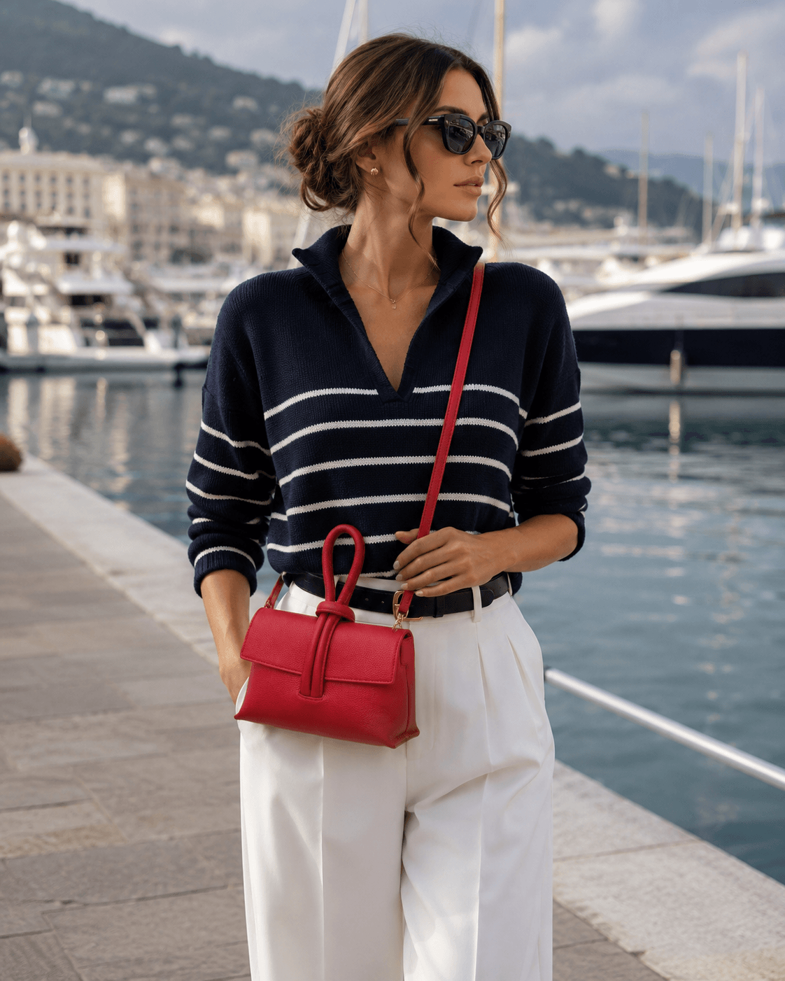 Clutch Michelle Rosso – Frau trägt rote Leder Clutch als Umhängetasche, eleganter Streetstyle Look mit Marinepullover und weißer Hose am Hafen
