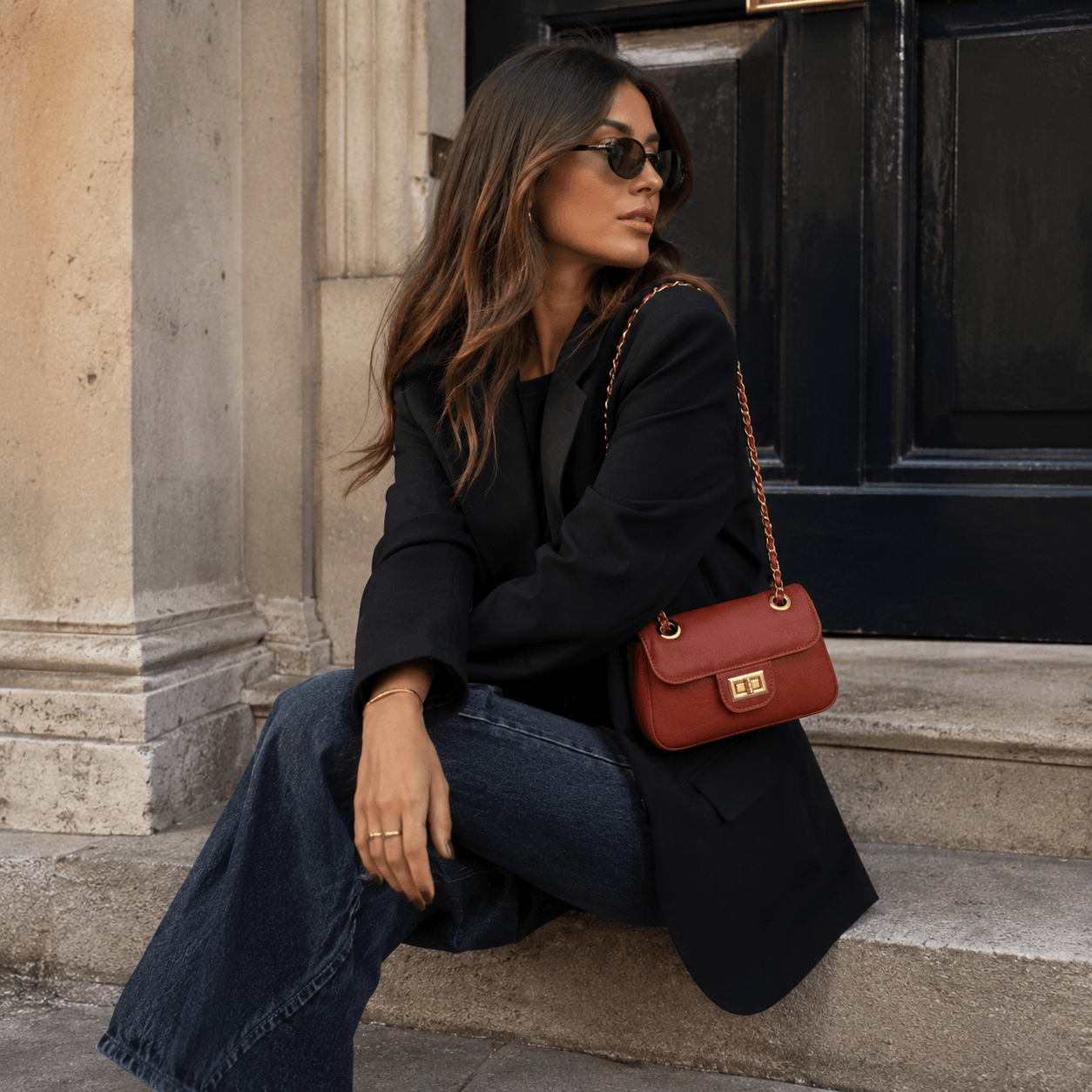 Clutch Nora Red – LiBEAU Damen trägt rostrote Leder-Clutch an Goldkette zu schwarzem Oversized-Blazer und dunkelblauen Wide-Leg-Jeans auf Pariser Treppe, zeitloser selbstbewusster Herbst City Look | LiBEAU
