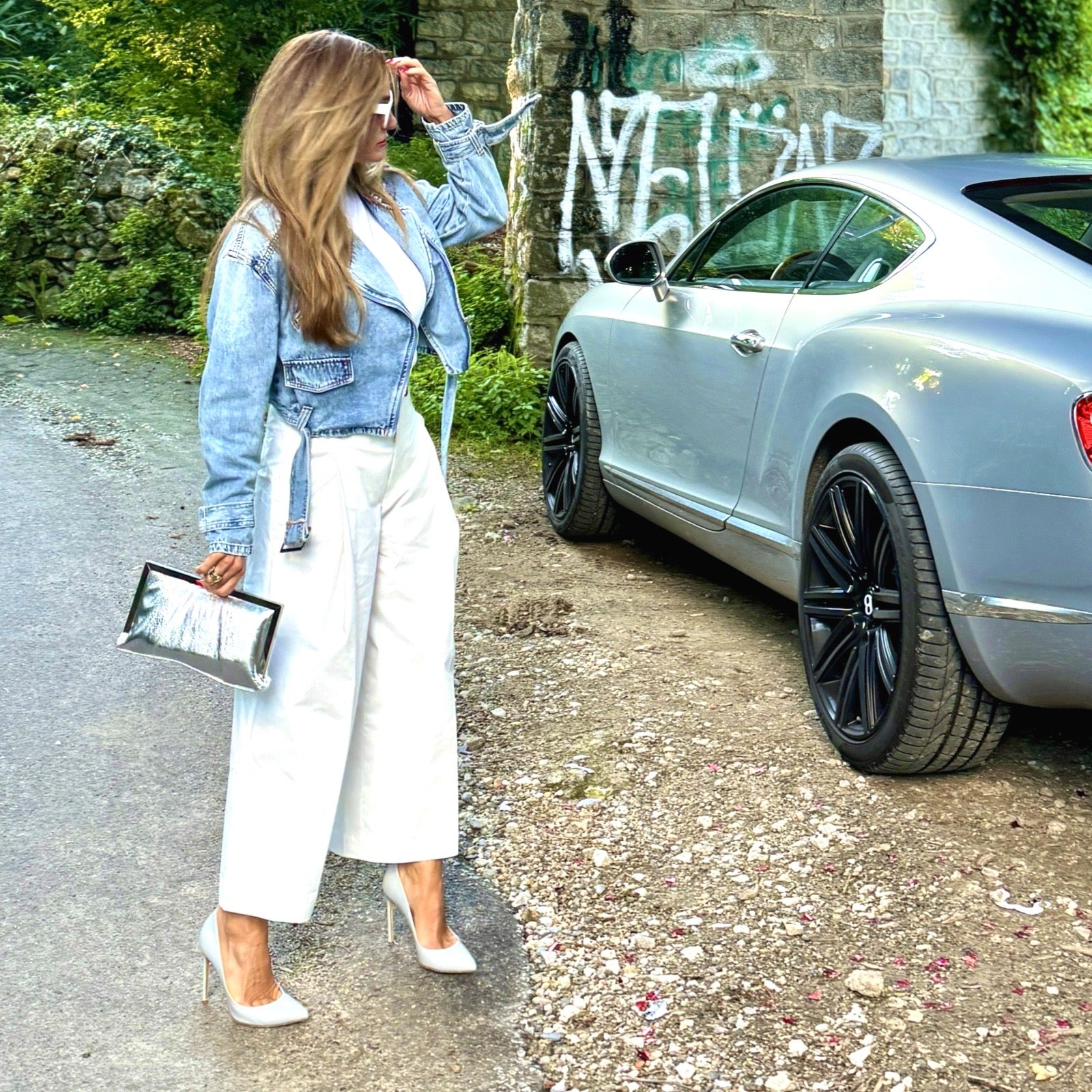 Wedding Clutch Silver – Frau trägt silberne Clutch zum weißen Culotte-Look mit Jeansjacke und weißen Pumps neben einem silbernen Bentley | LiBEAU
